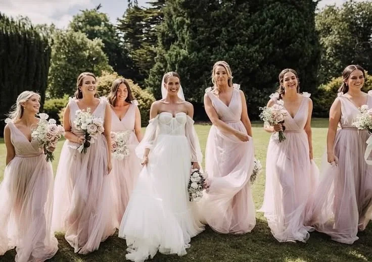Bride walking with bridesmaids in soft blush gowns through a garden