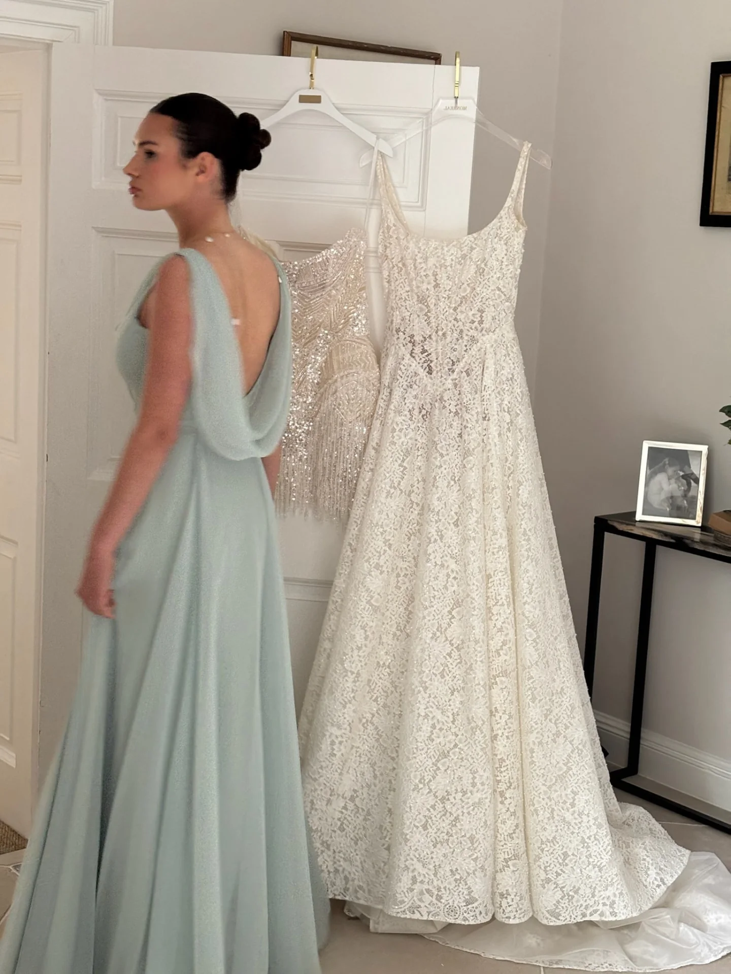 Woman wearing a pale blue draped bridesmaid gown beside bridal dresses