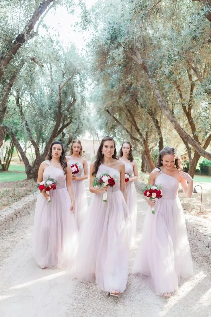 Bridesmaids wearing pale lavender one-shoulder gowns beneath olive trees