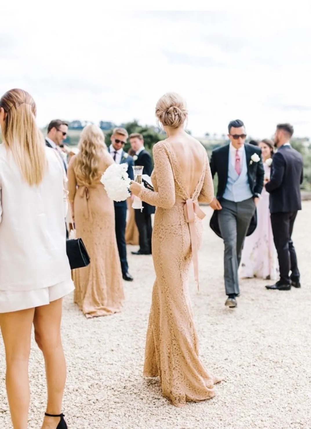 Wedding guest wearing a blush lace gown with a ribbon-tied open back