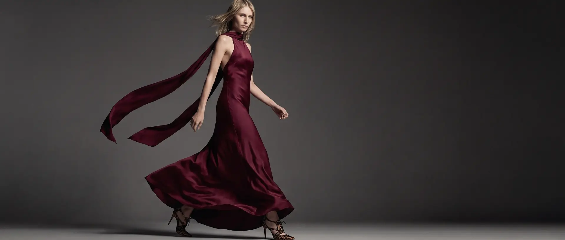 Model wearing a flowing burgundy satin evening gown by Kitty Dickerson-Firth