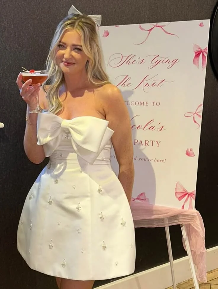 Woman wearing an embellished ivory bridal mini dress with an oversized bow