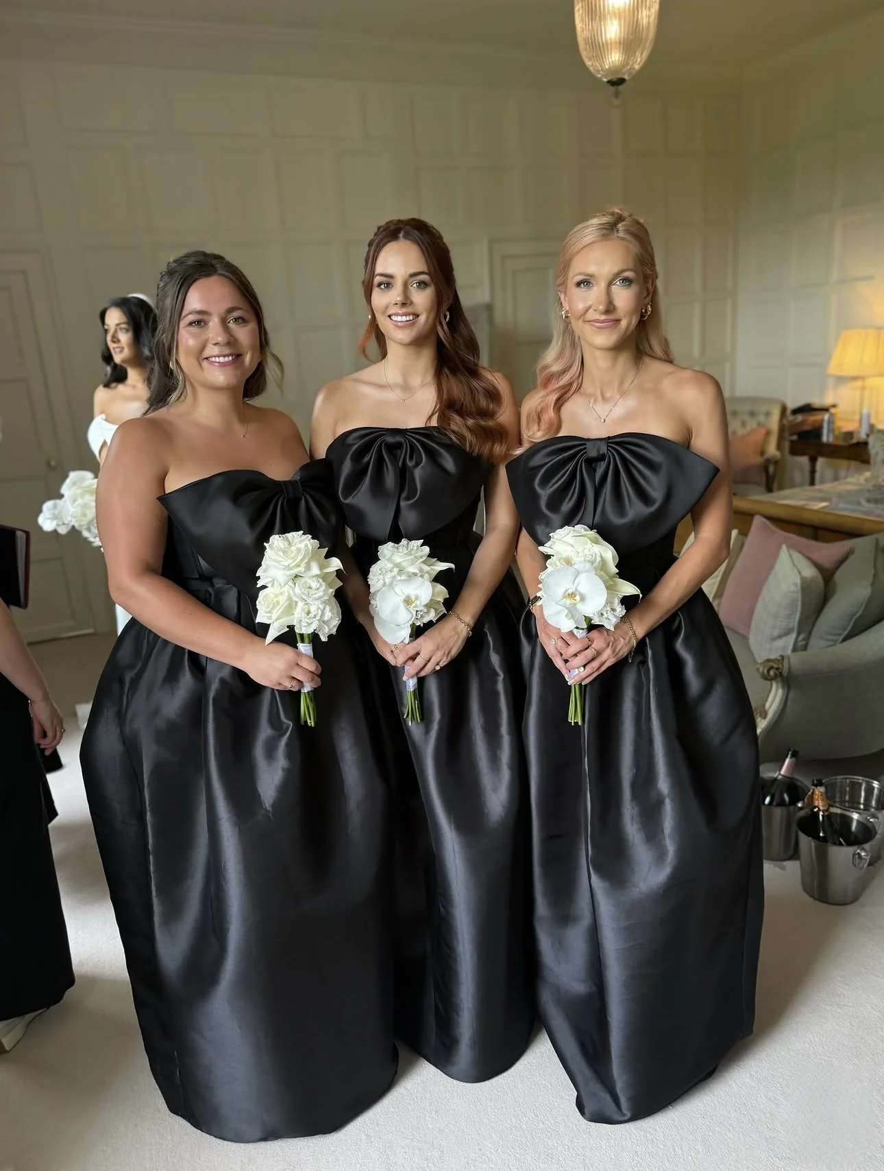 Three bridesmaids wearing black satin gowns with sculptural bow bodices